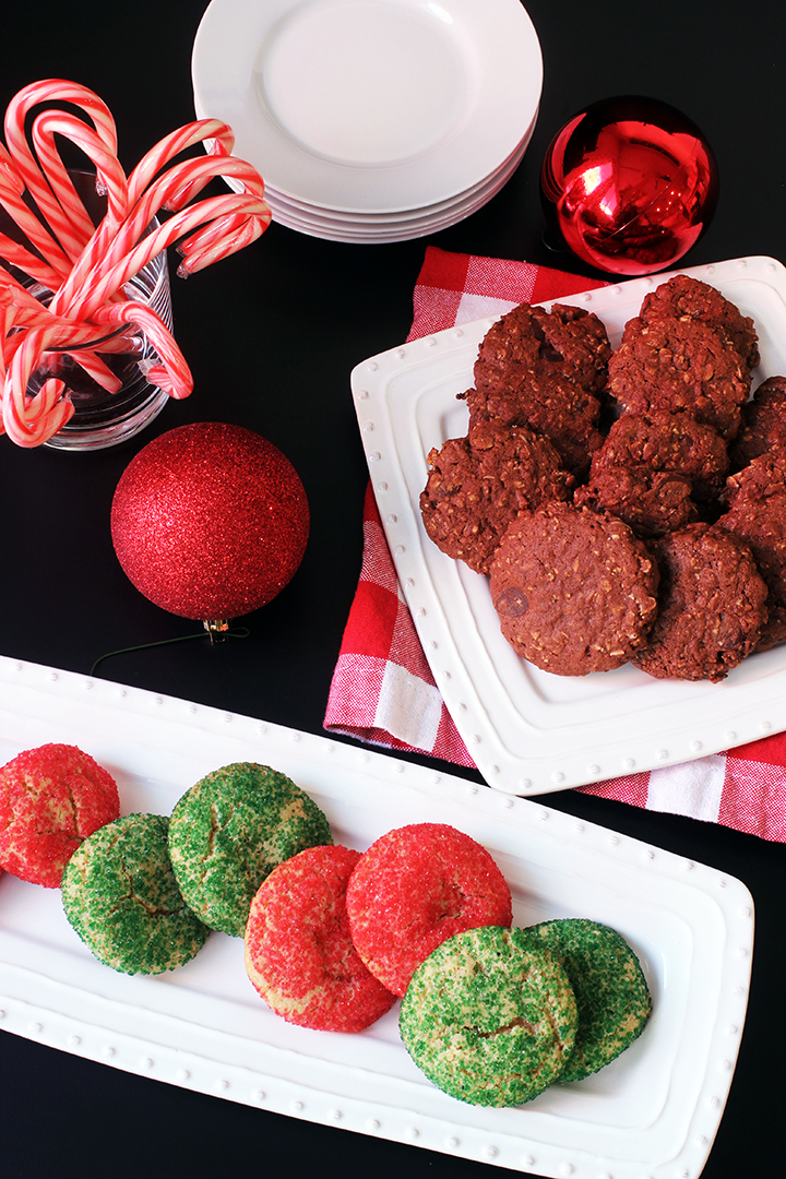 Platters of Christmas cookies on a black table with ornaments and candy canes.