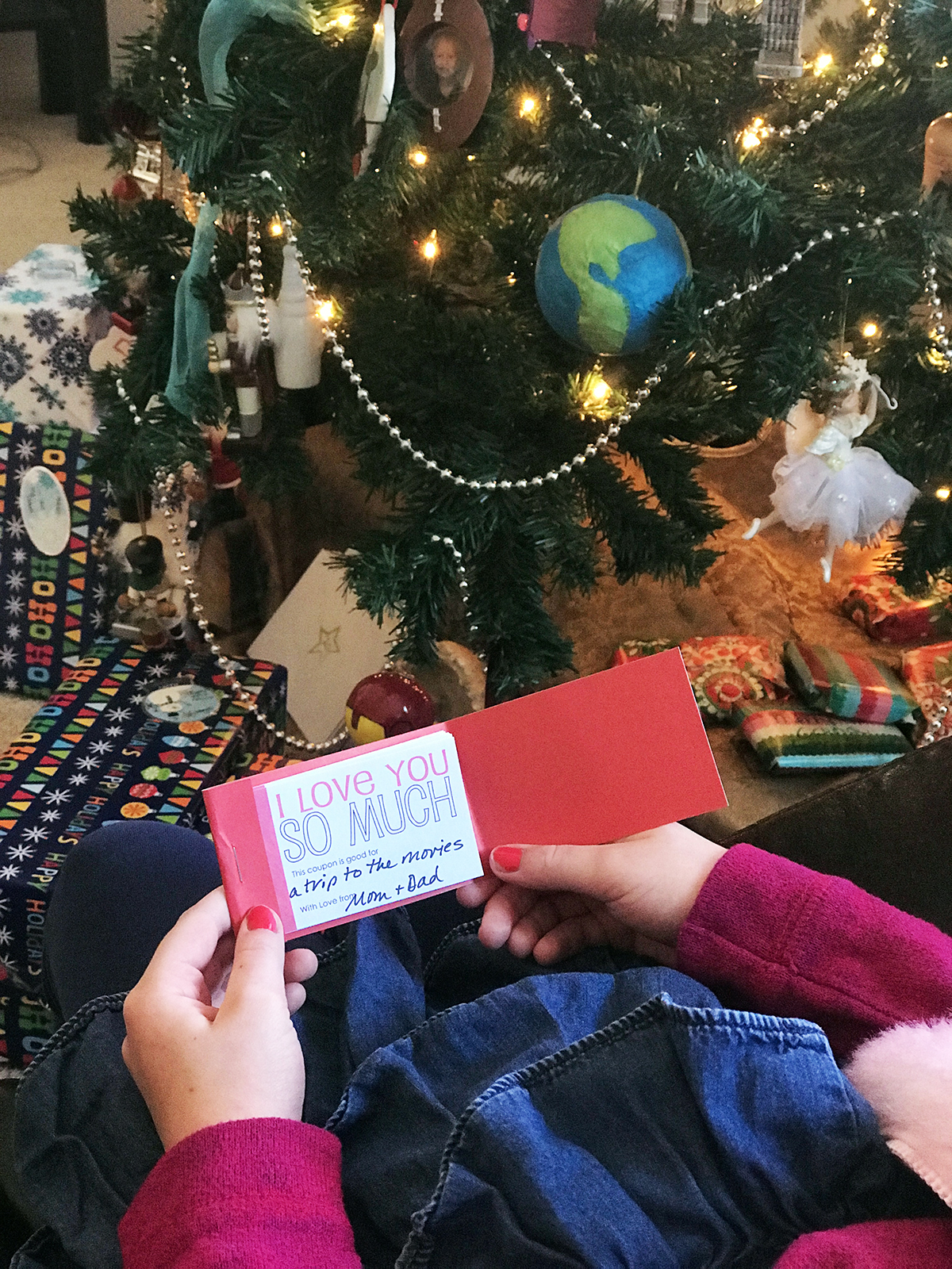 girl holding coupon book as she sits by christmas tree
