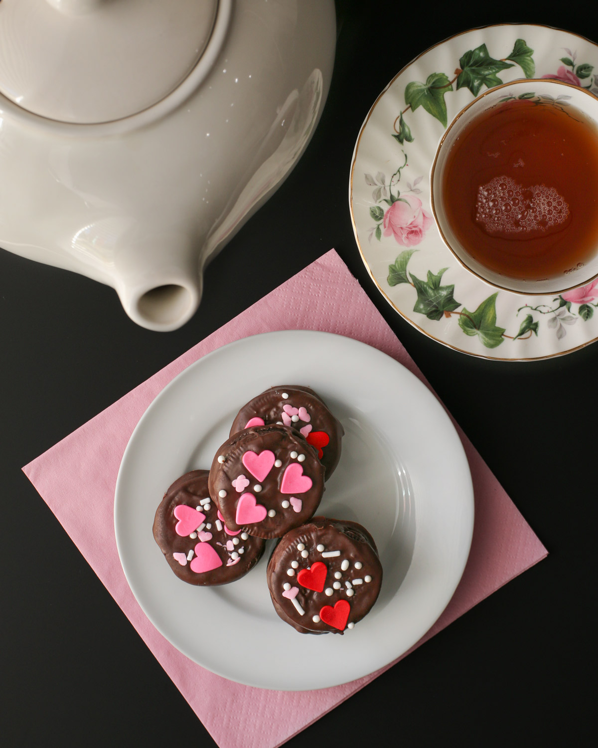 tea pot near cup of tea by plate of valentine oreos.