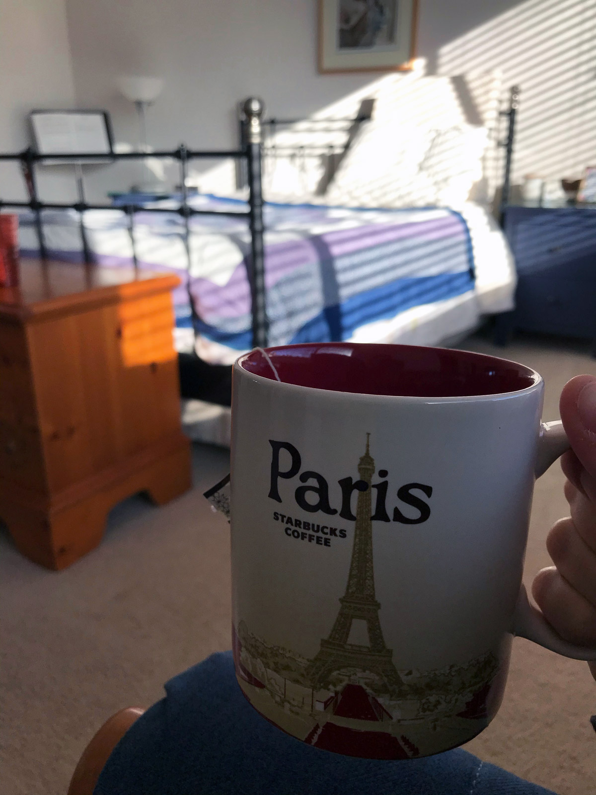 holding paris mug with bed in background