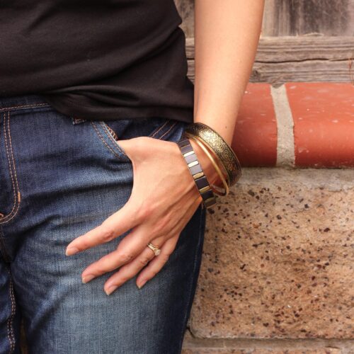 a woman's arm strung with bracelets, her thumb hooked in the pocket of her jeans.