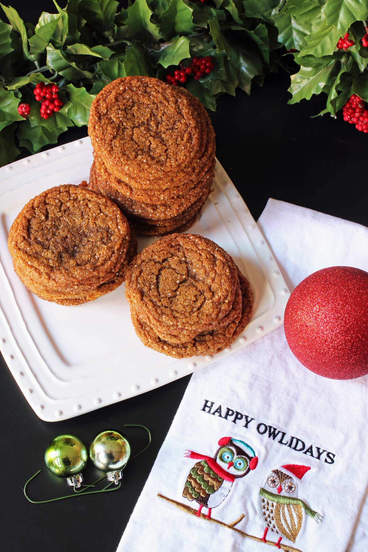 stack of gingerbread crinkles on a white square plate near a towel with owls on it that says Happy Owlidays.