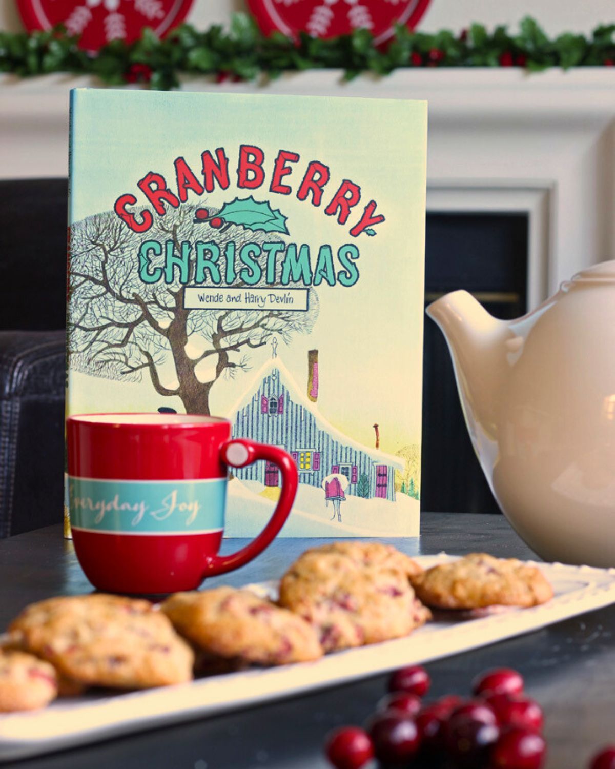 cranberry christmas book standing up on table with cranberry cookies on platter with mug and tea pot.