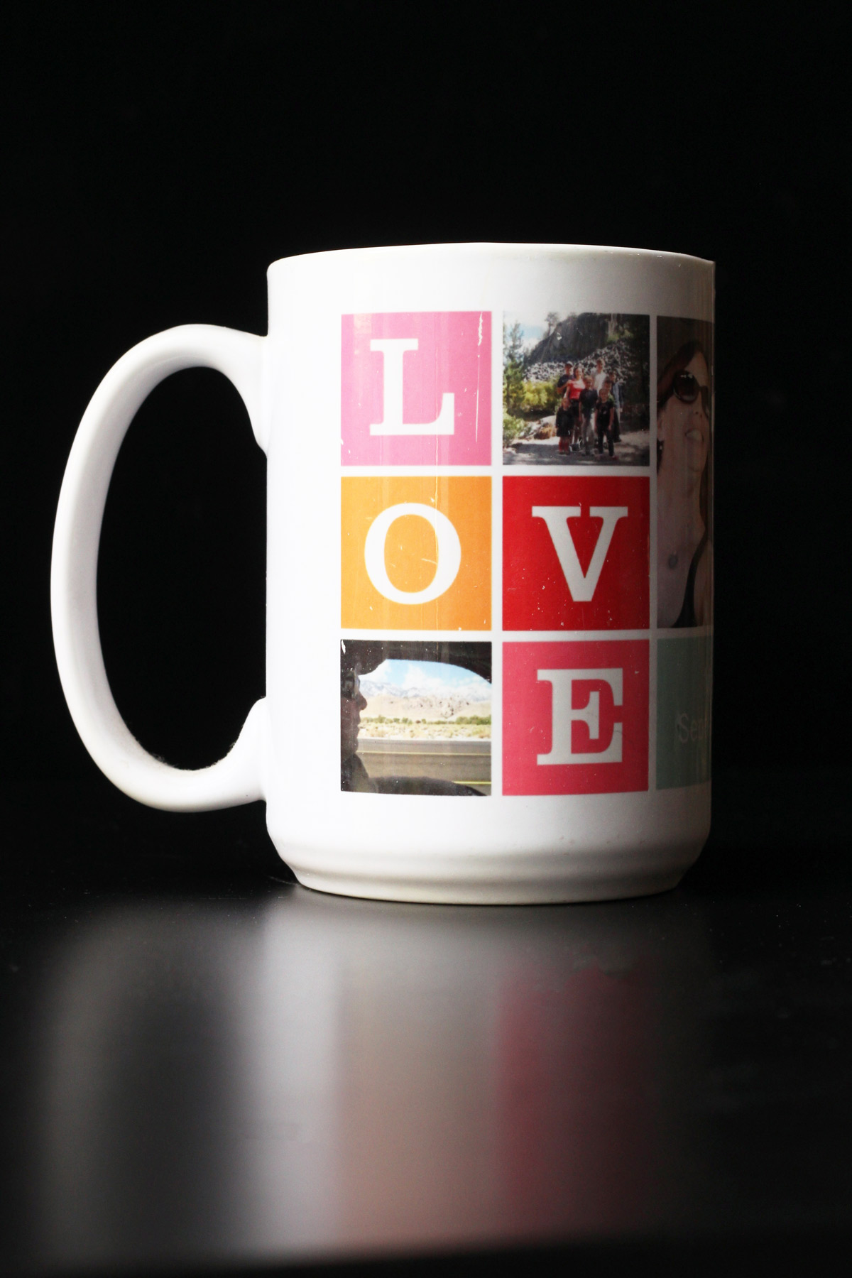 white photo mug with a pink and orange collage of the letters LOVE on a black table top with a black background