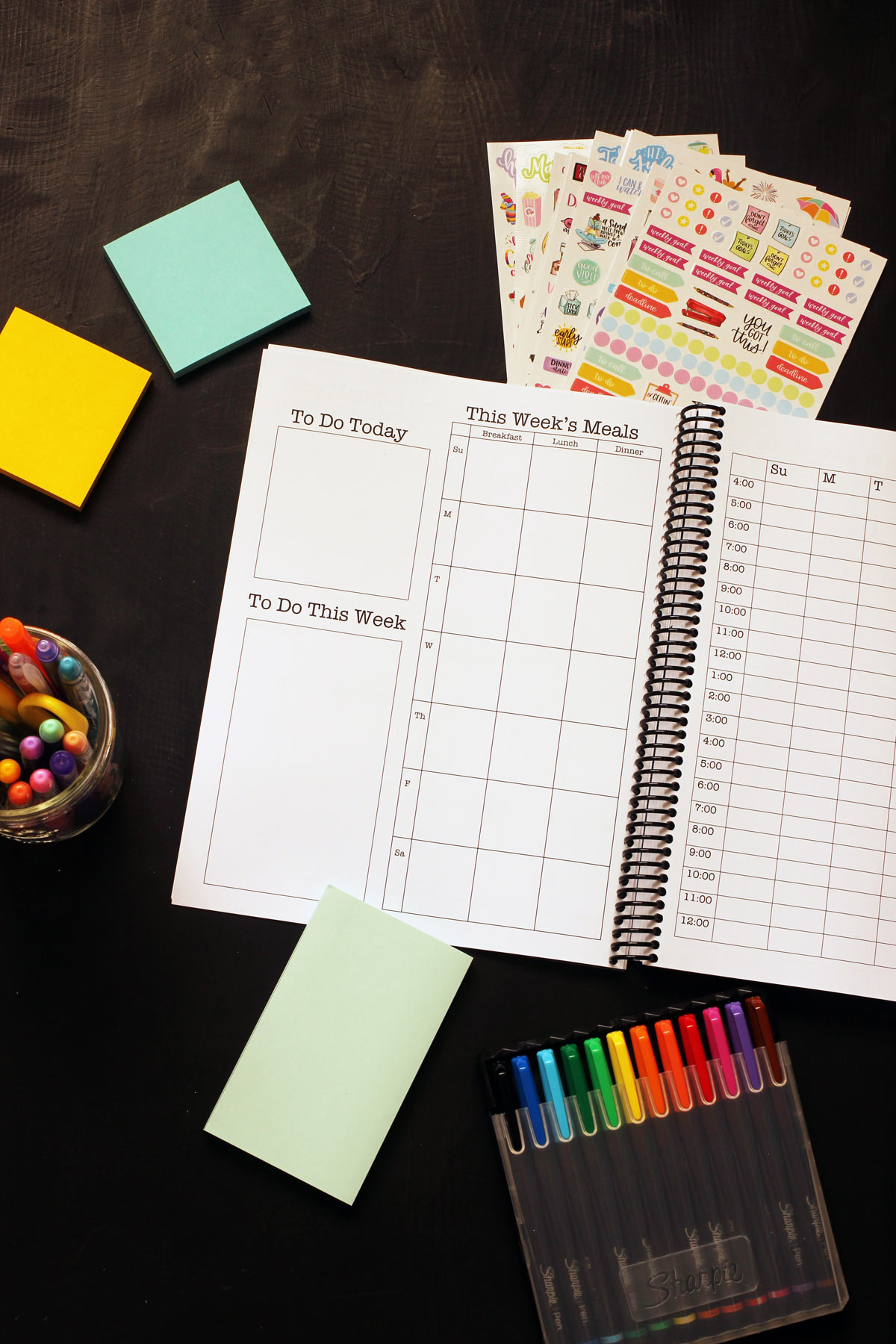 planner with post-its, pens, and markers open on a black table, showing the weekly to do page.