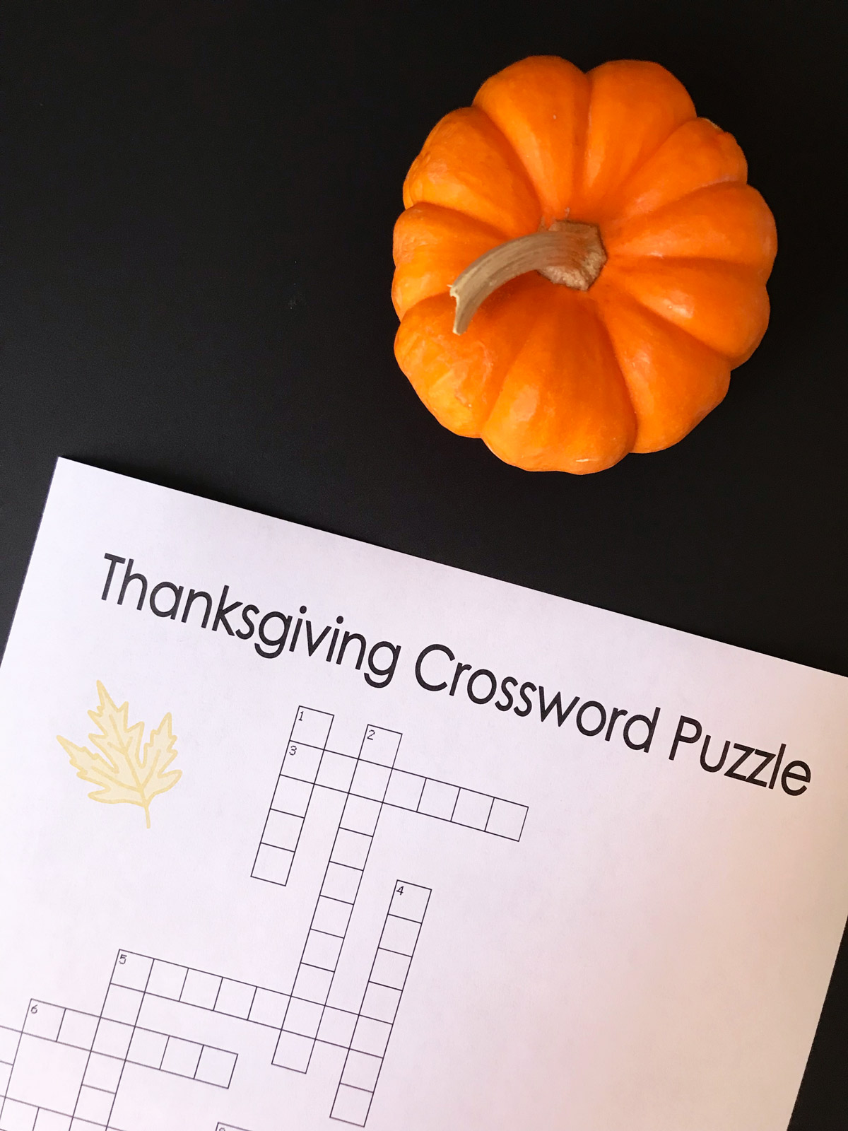 mini pumpkin on table next to thanksgiving crossword puzzle.