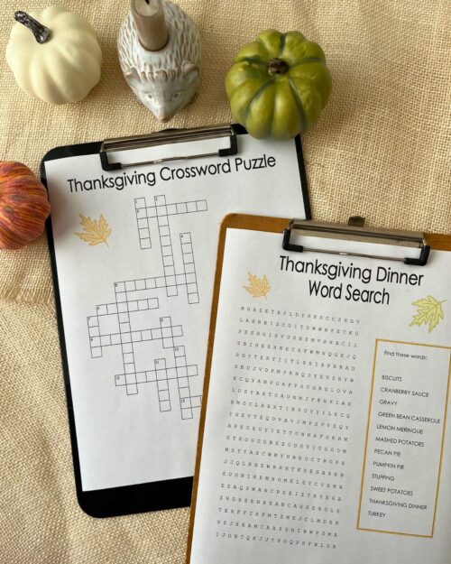 Thanksgiving crossword puzzle and Thanksgiving word search on clipboards with fall decor on table nearby.