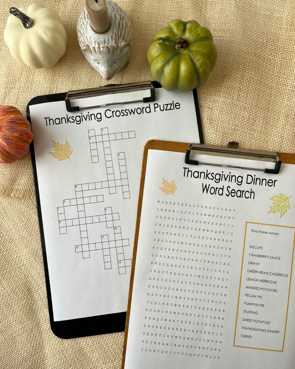 Thanksgiving crossword puzzle and Thanksgiving word search on clipboards with fall decor on table nearby.