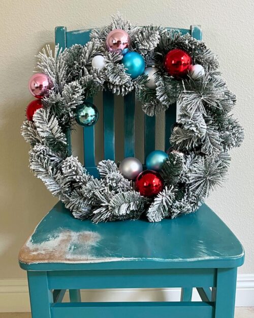 flocked wreath with 50s color themed ornaments sitting on weather-beaten chair.