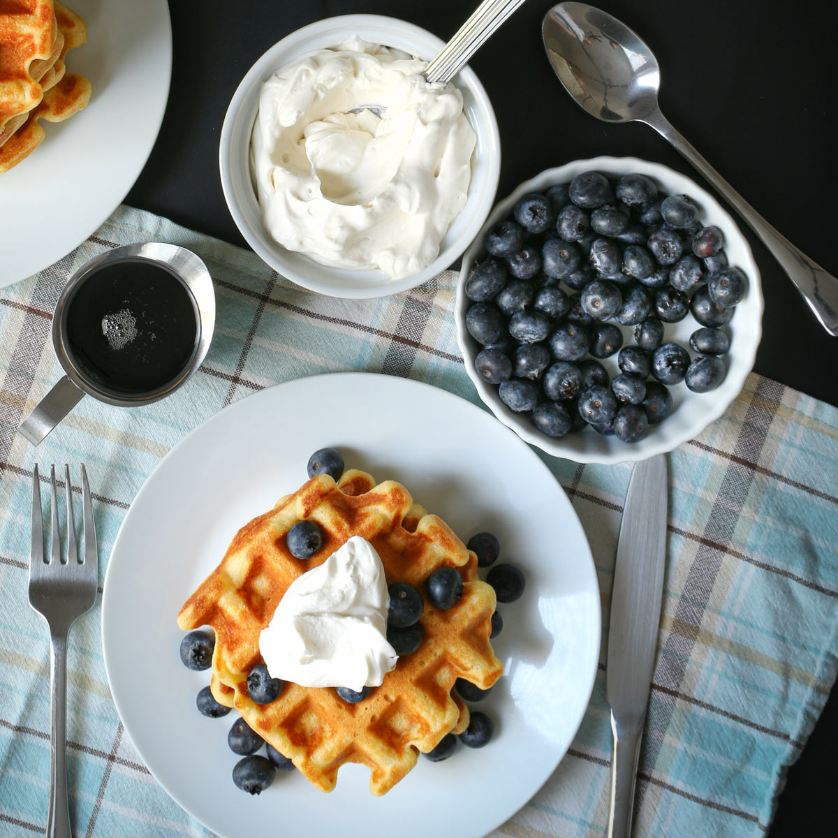 stack of waffles on plate with whipped cream and blueberries.