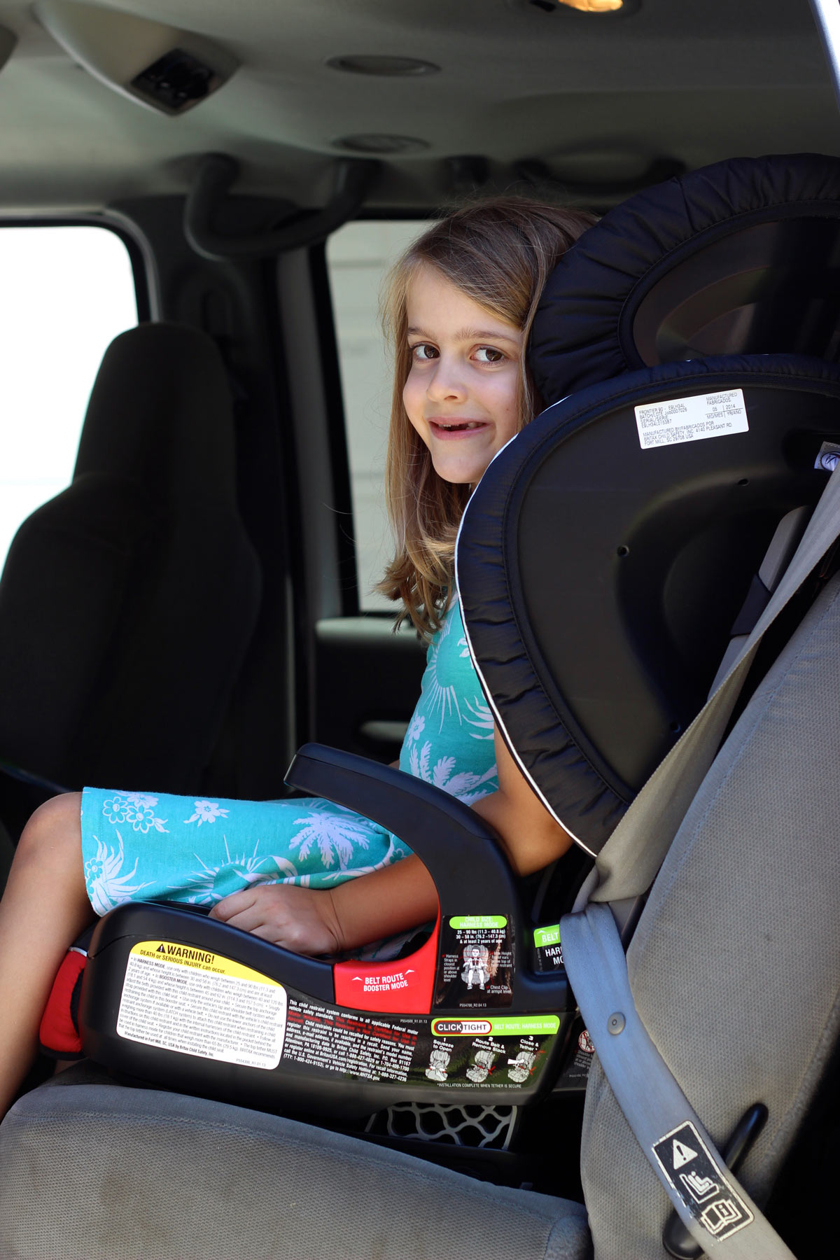 girl strapped into booster seat in car, looking out the open door.