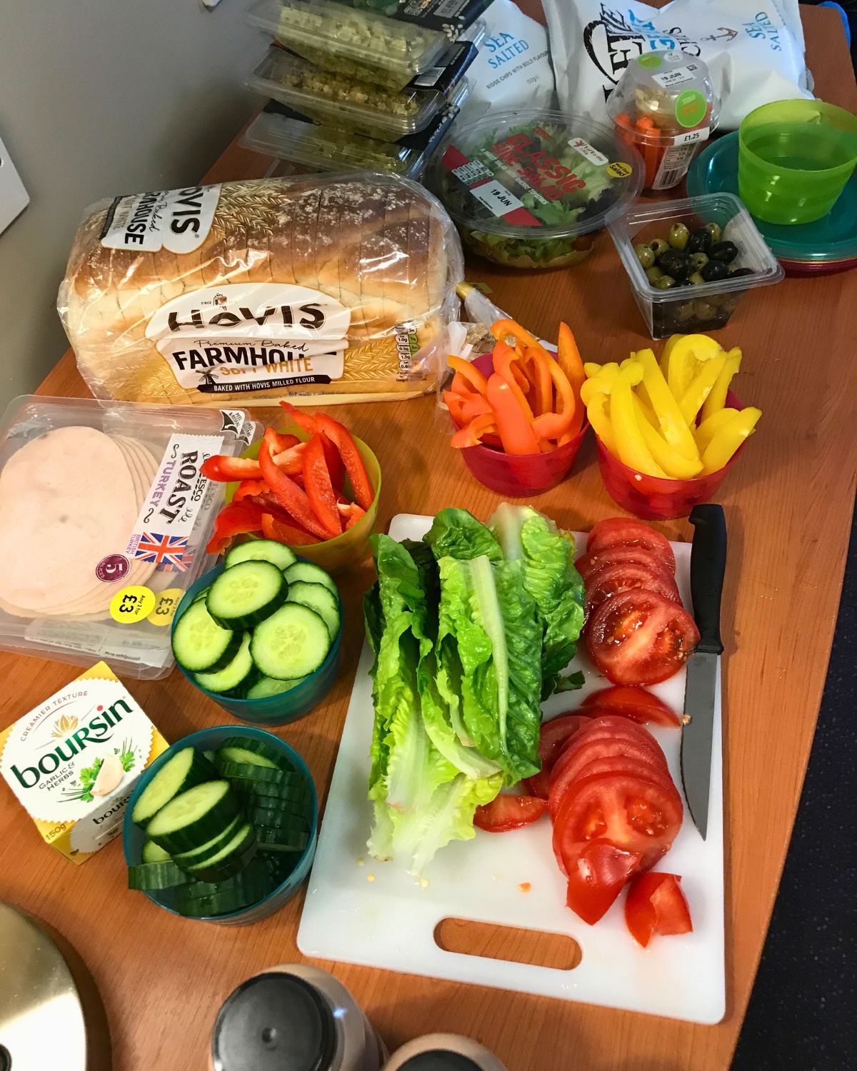 cutting board and knife with prepped veggies and sandwich fixings on hotel table.