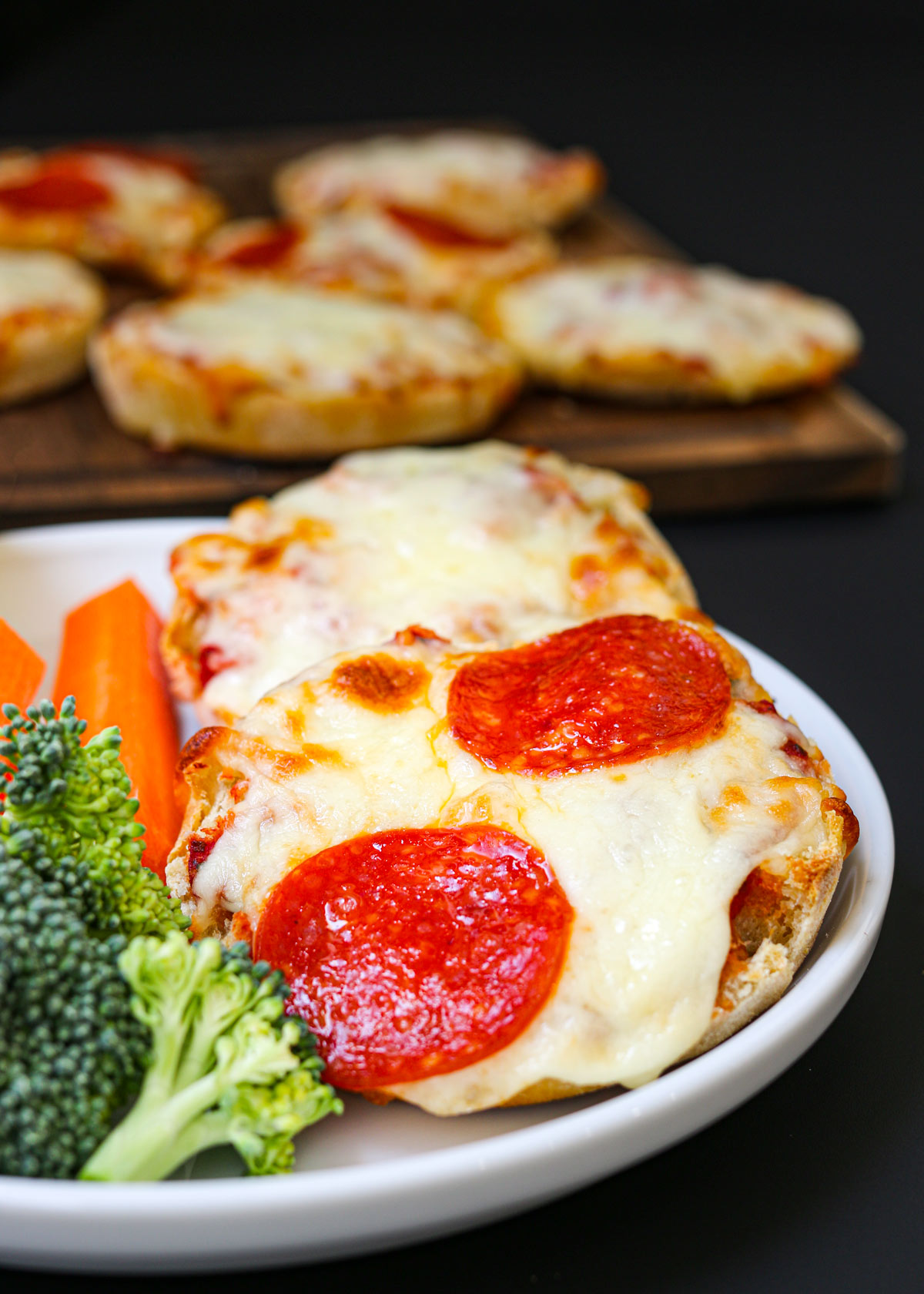 English muffin pizzas on a plate with veggies.