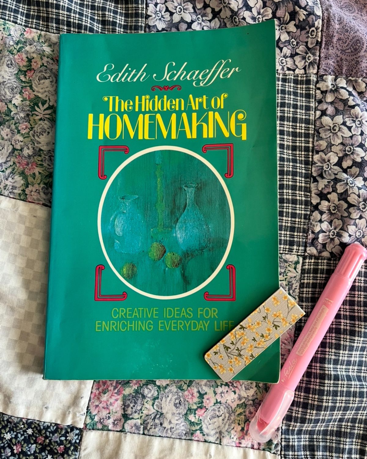 paperback copy of the hidden art of homemaking on quilt with highlighter and bookmark magnet.