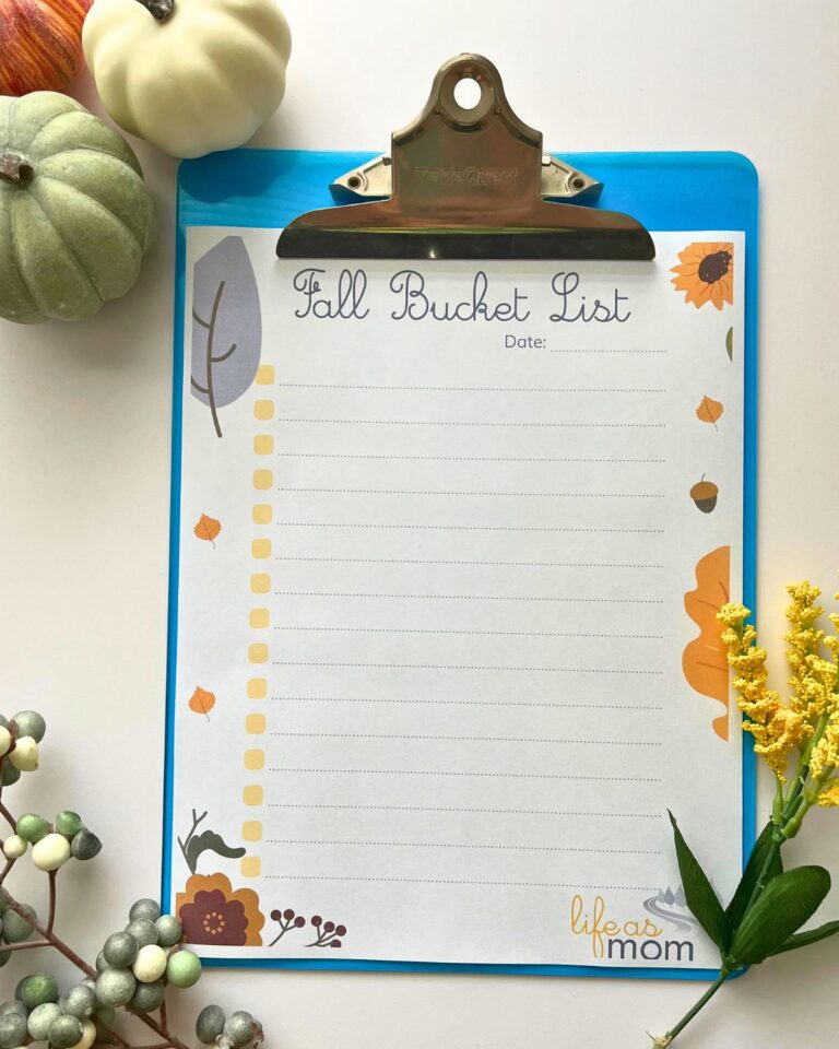 paper fall bucket list on clipboard surrounded by fall foliage and small pumpkins.