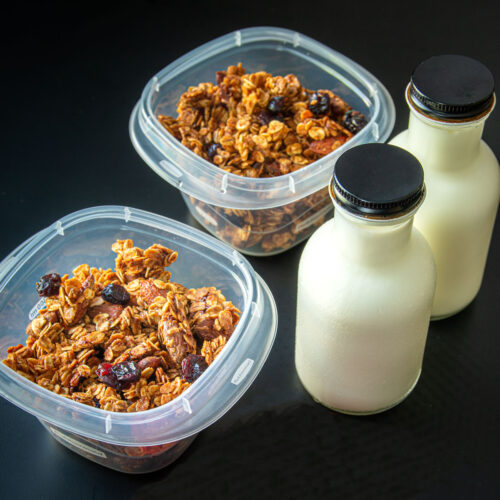 meal prep boxes with granola next to two bottles of milk.