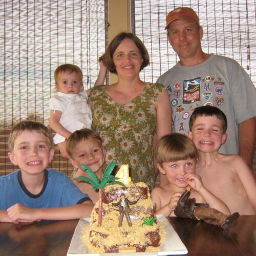 mom, dad, and kids around kitchen table with birthday cake in center.