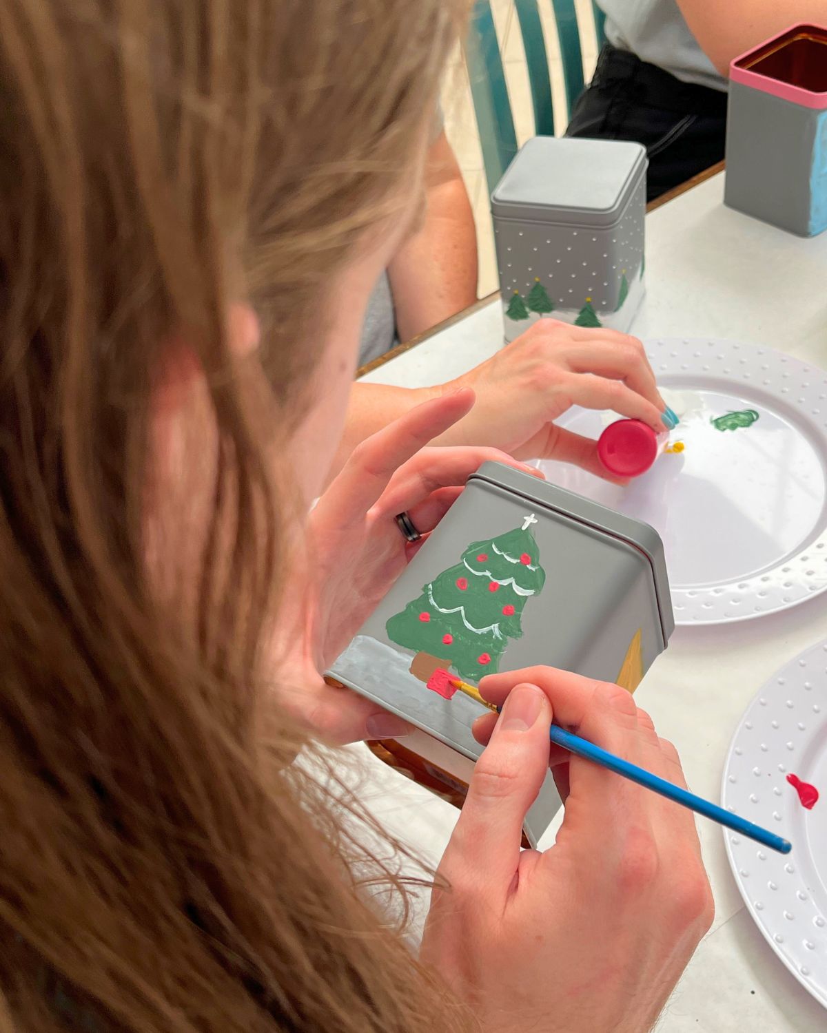 side view of man painting a christmas tree on a tea tin.