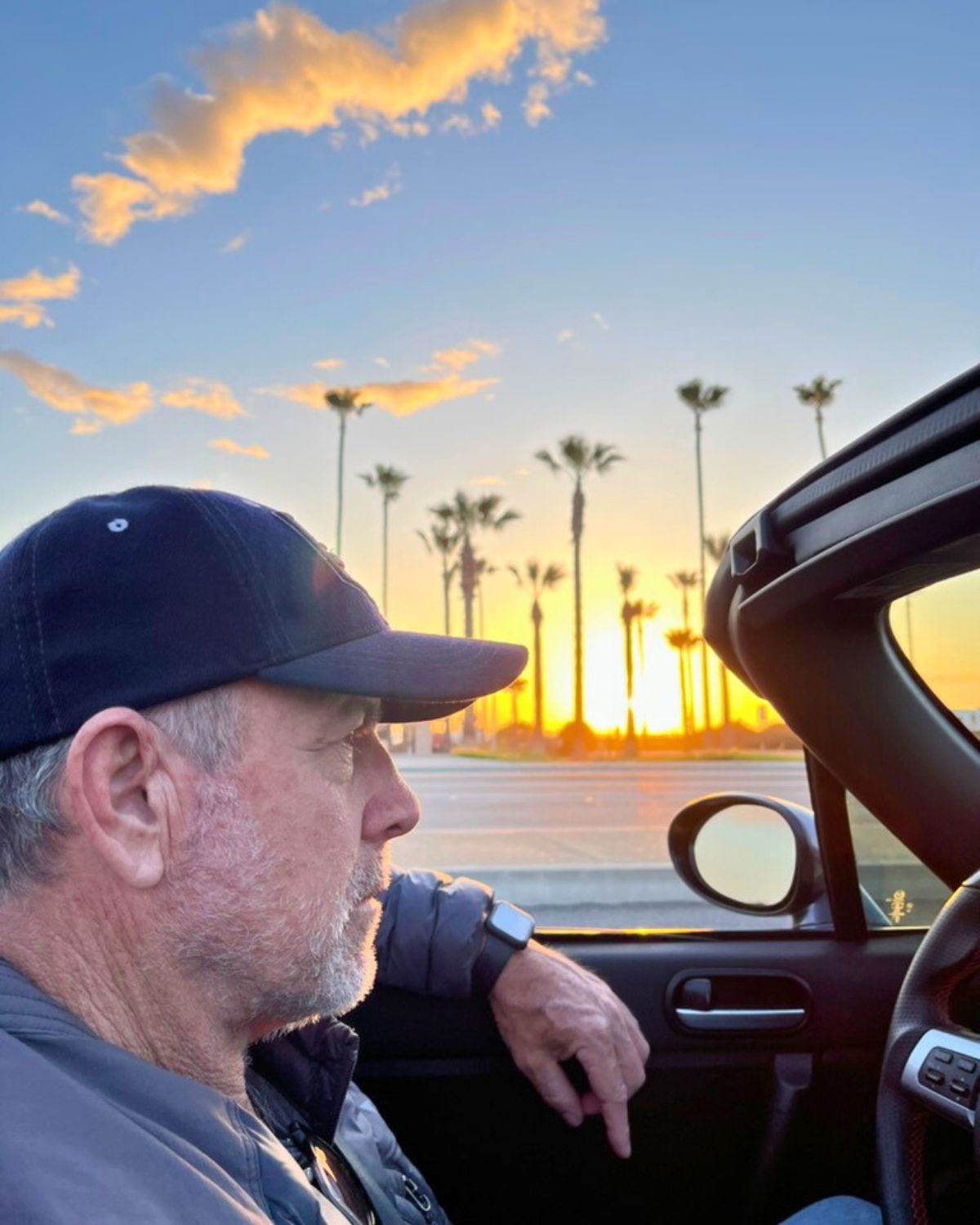 bryan driving the convertible with palm trees and sunset in the background.