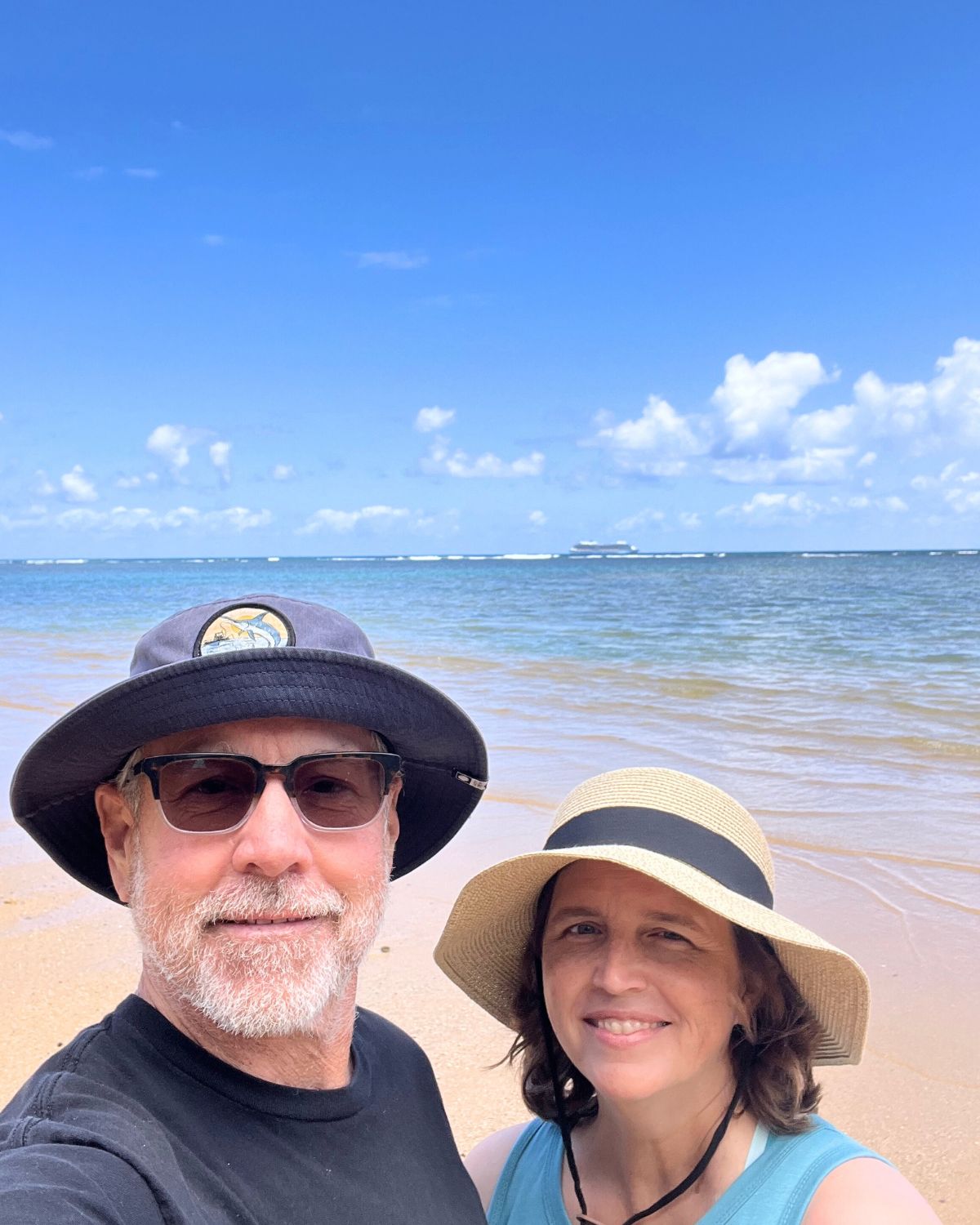 bryan and jessica on anini beach in kauai with a cruise ship in the water on the horizon.