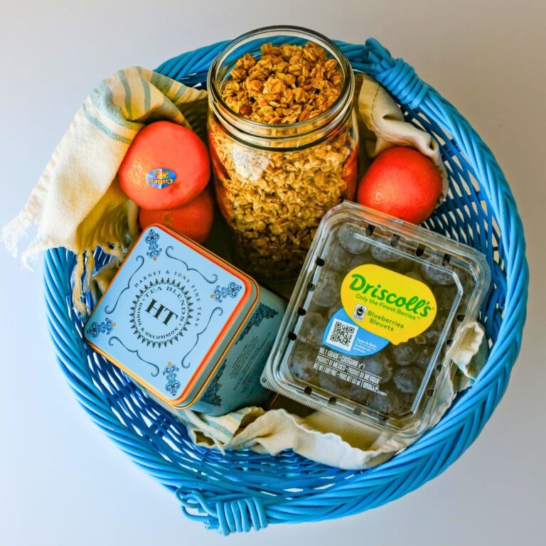 overhead shot of blue basket with a cloth, tea, fruit, and a jar of granola.
