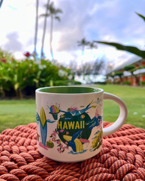 hawaii mug on a table with palm trees and clouds in the background.