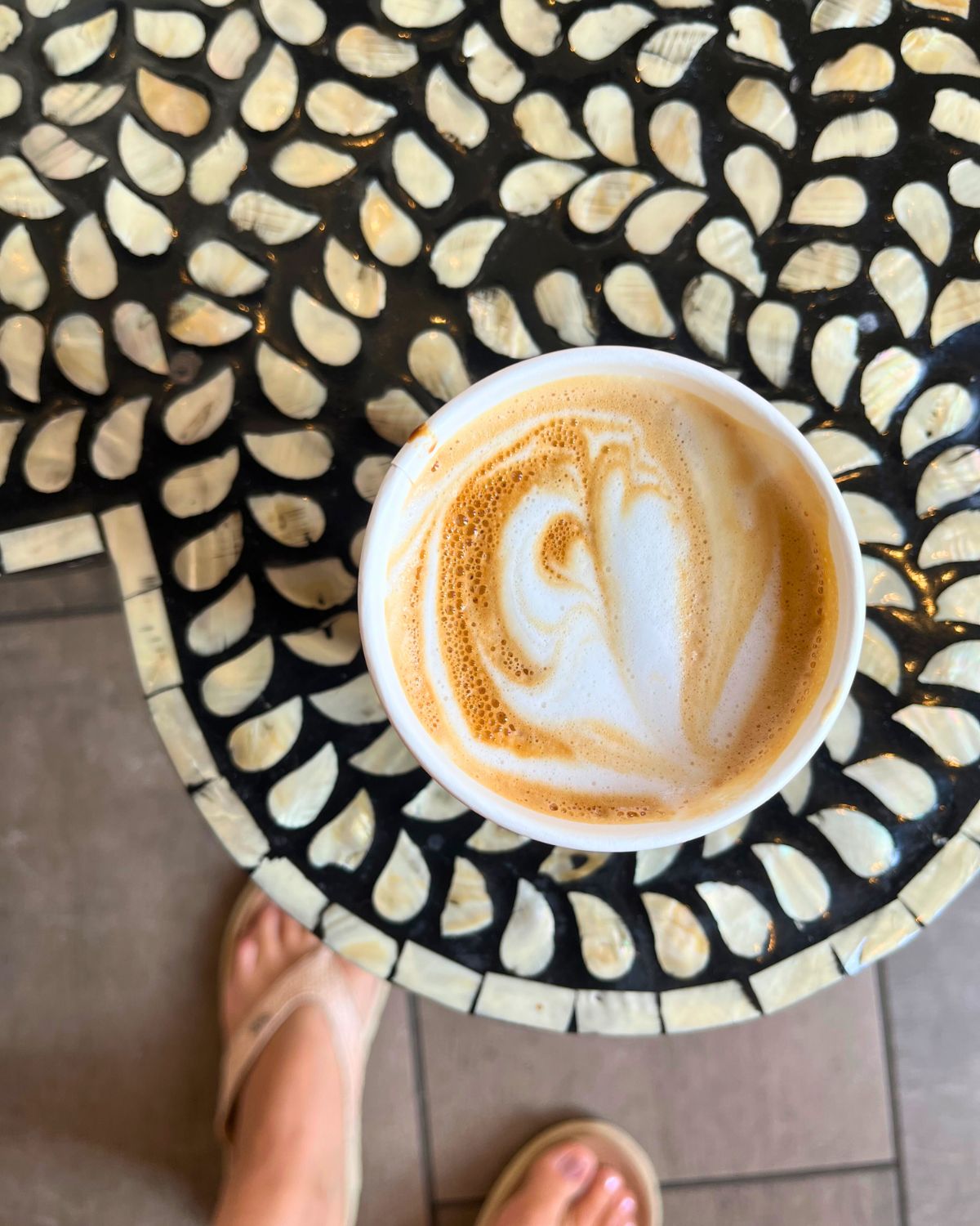 a flat white on a stone table with flip flop feet in the background.