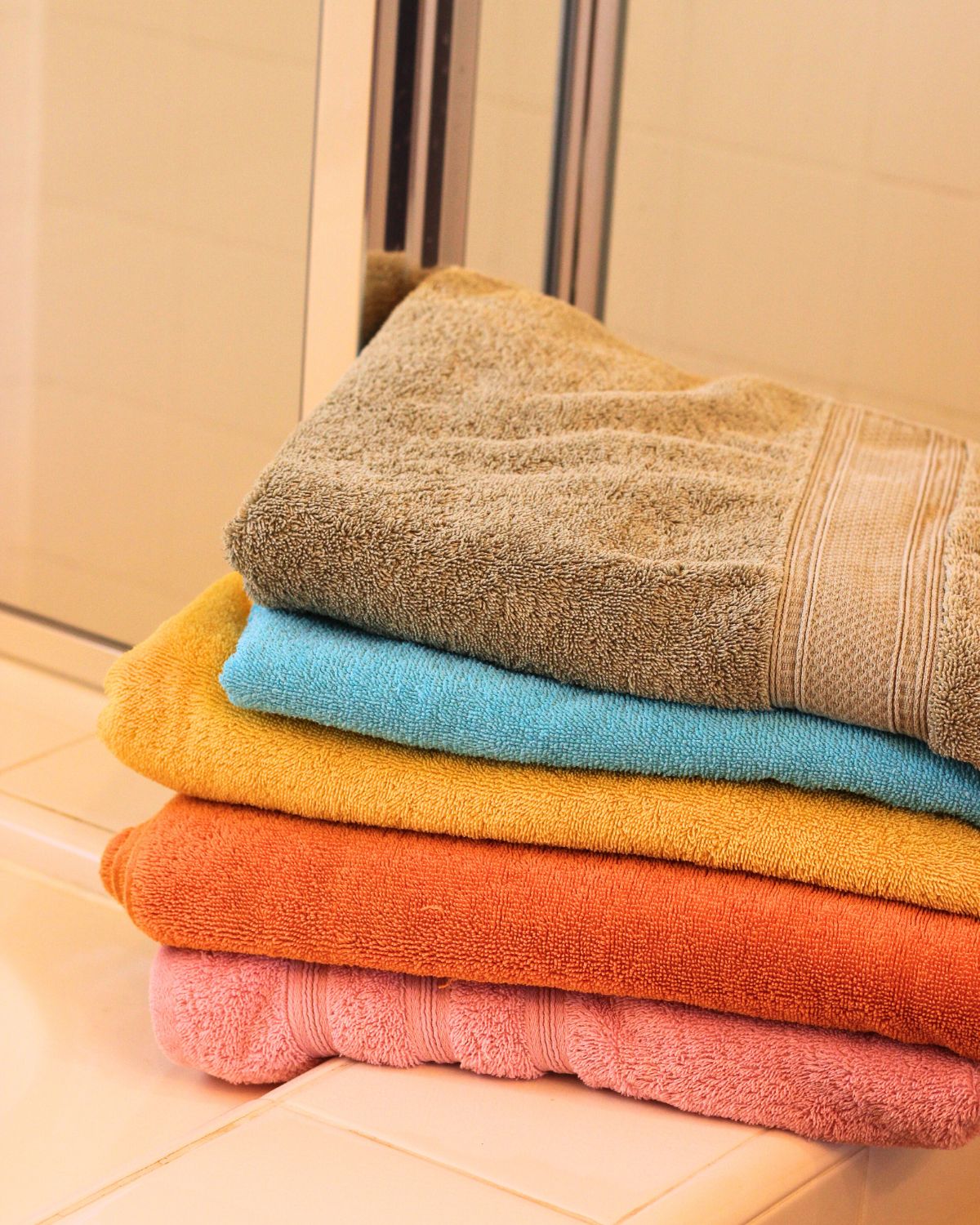 stack of multicolored towels folded on edge of bathtub.
