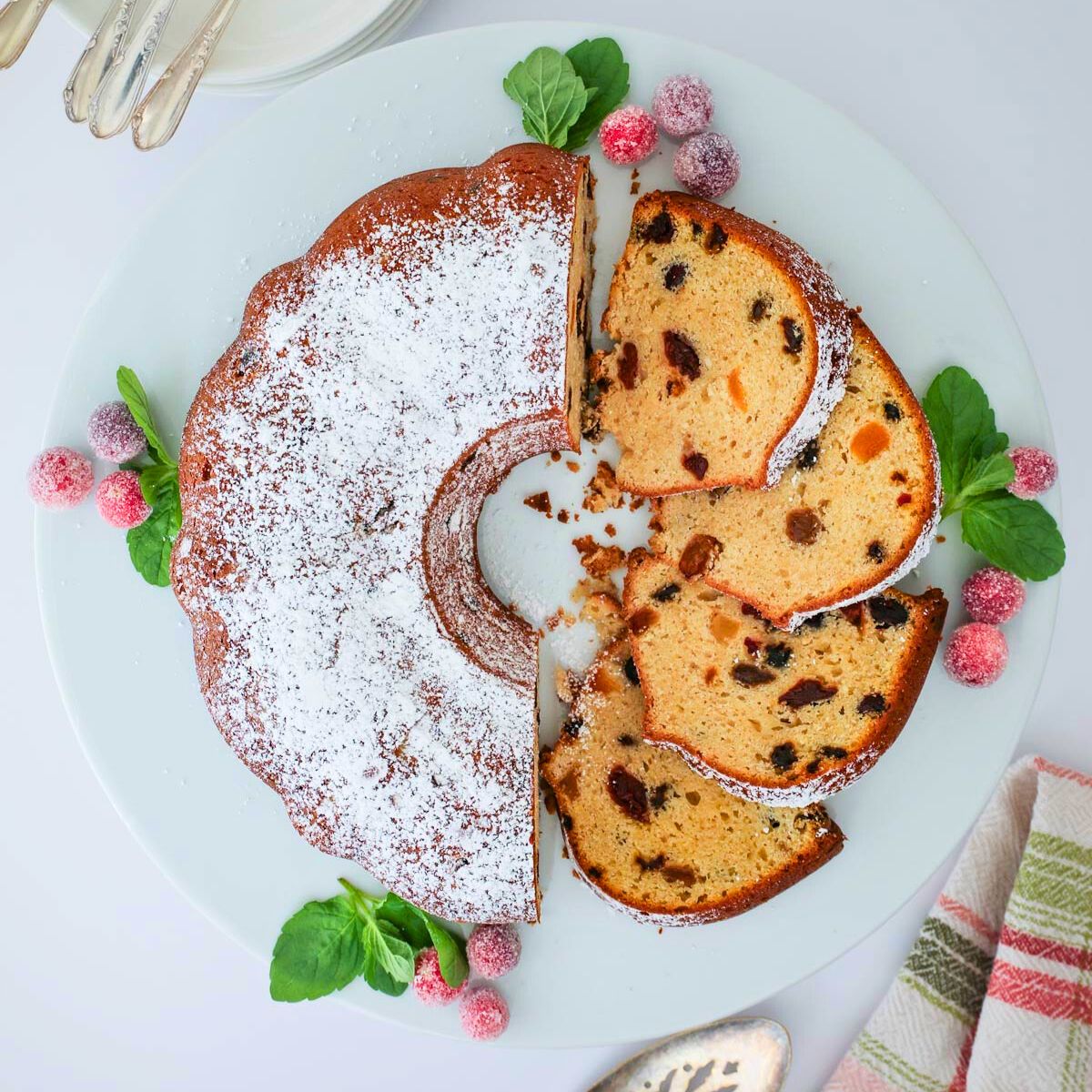 christmas bundt cake with sugared cranberries as garnish on platter, sliced.