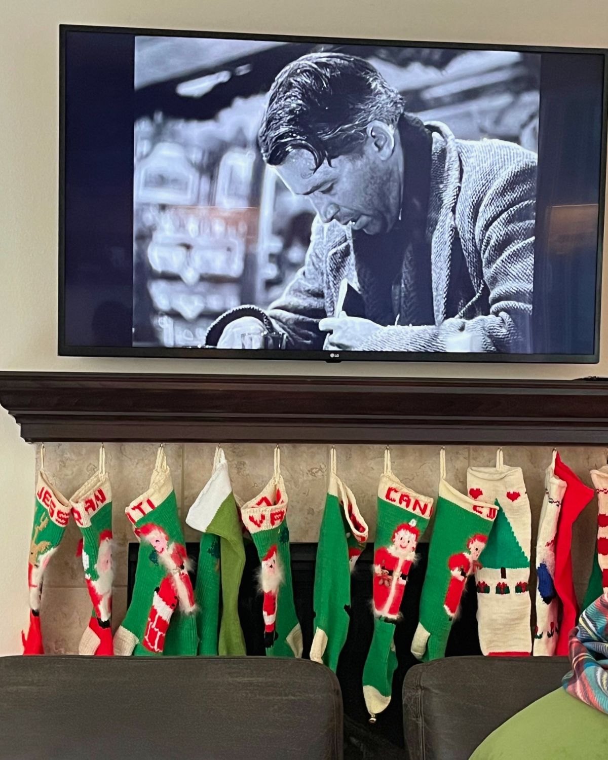 it's a wonderful life on the screen above the mantel with stockings hung beneath.