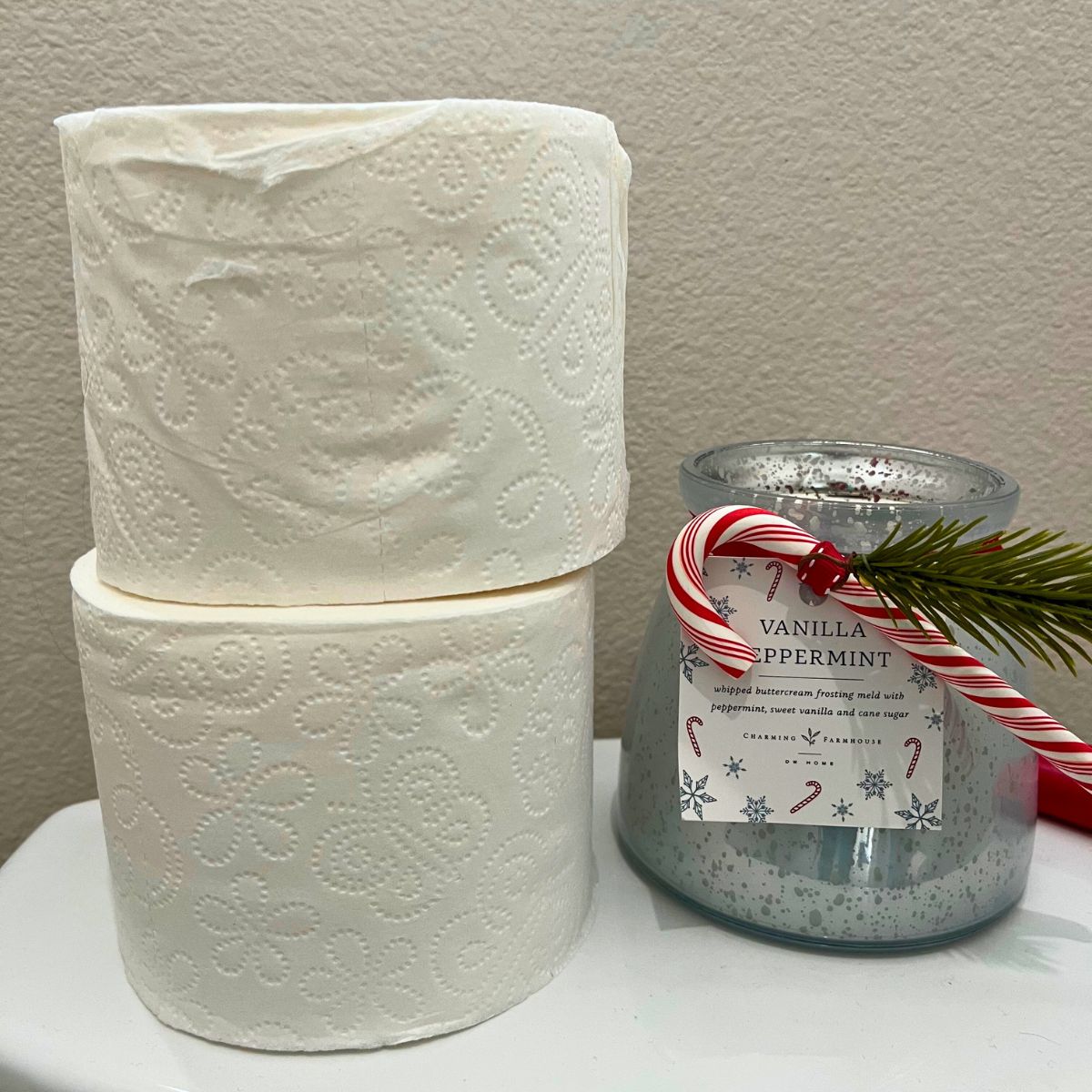 stack of toilet paper next to holiday candle on back of toilet.