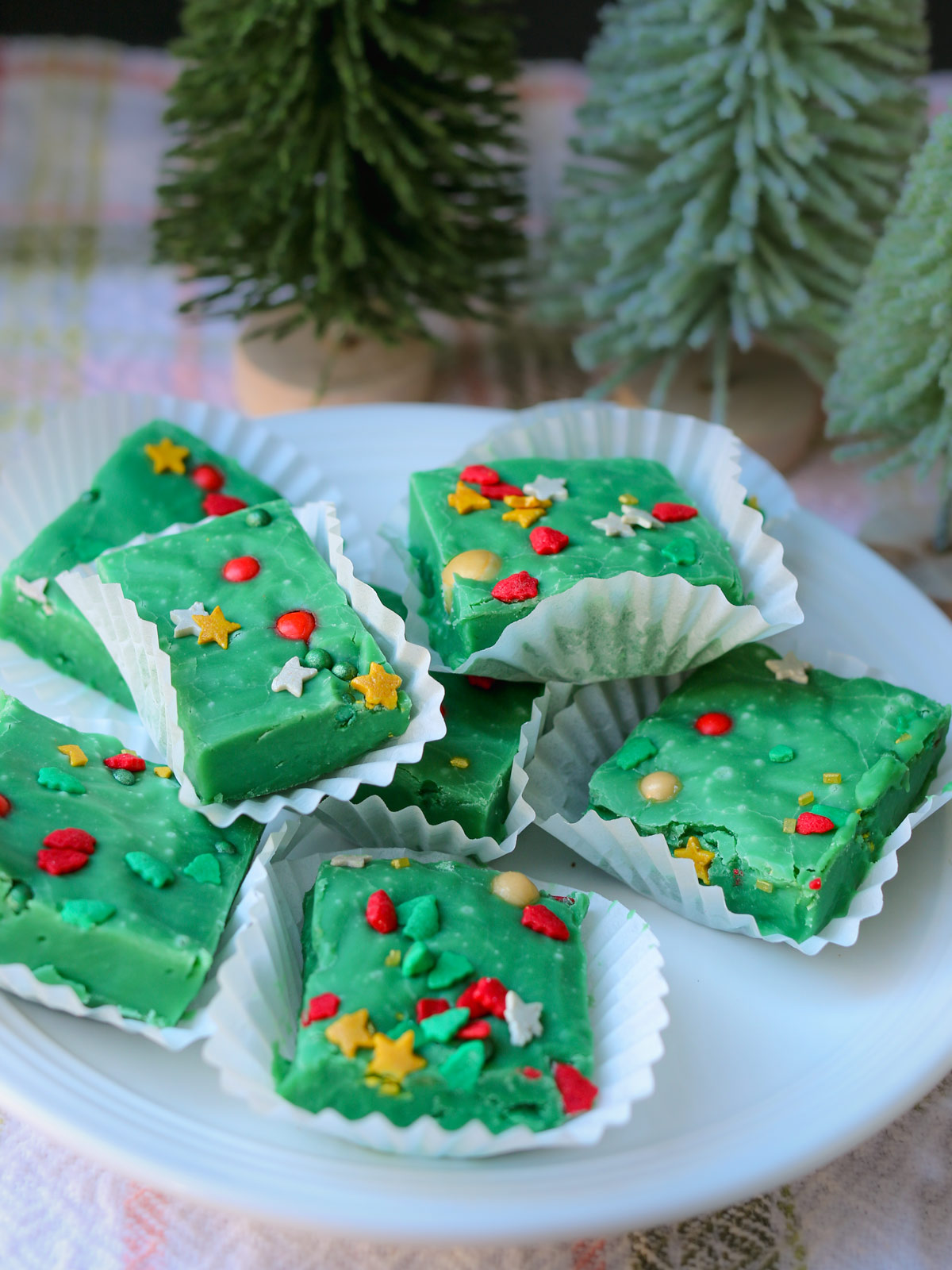 christmas fudge on plate with small trees nearby.