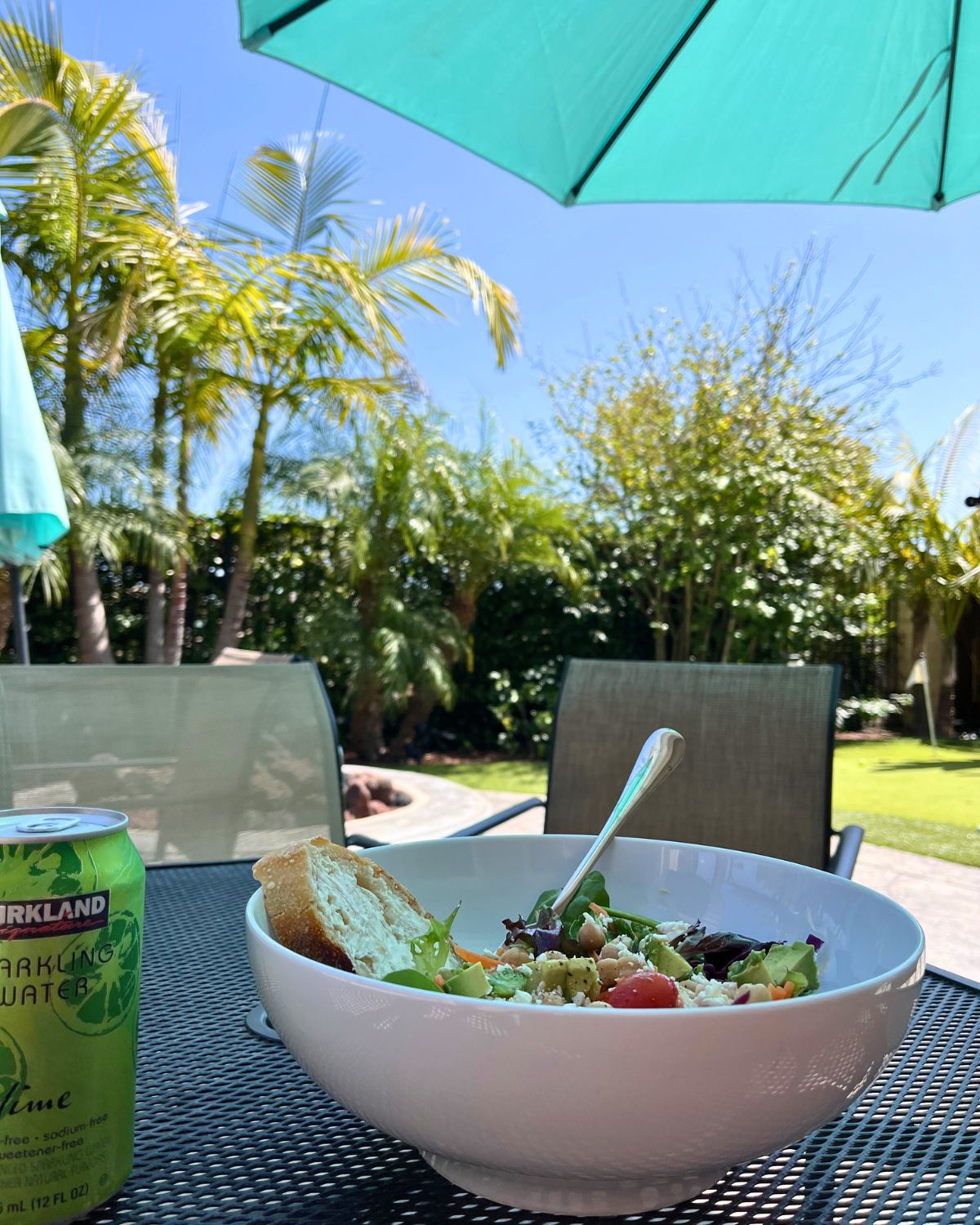 bowl of salad on table on patio with plants and blue sky.