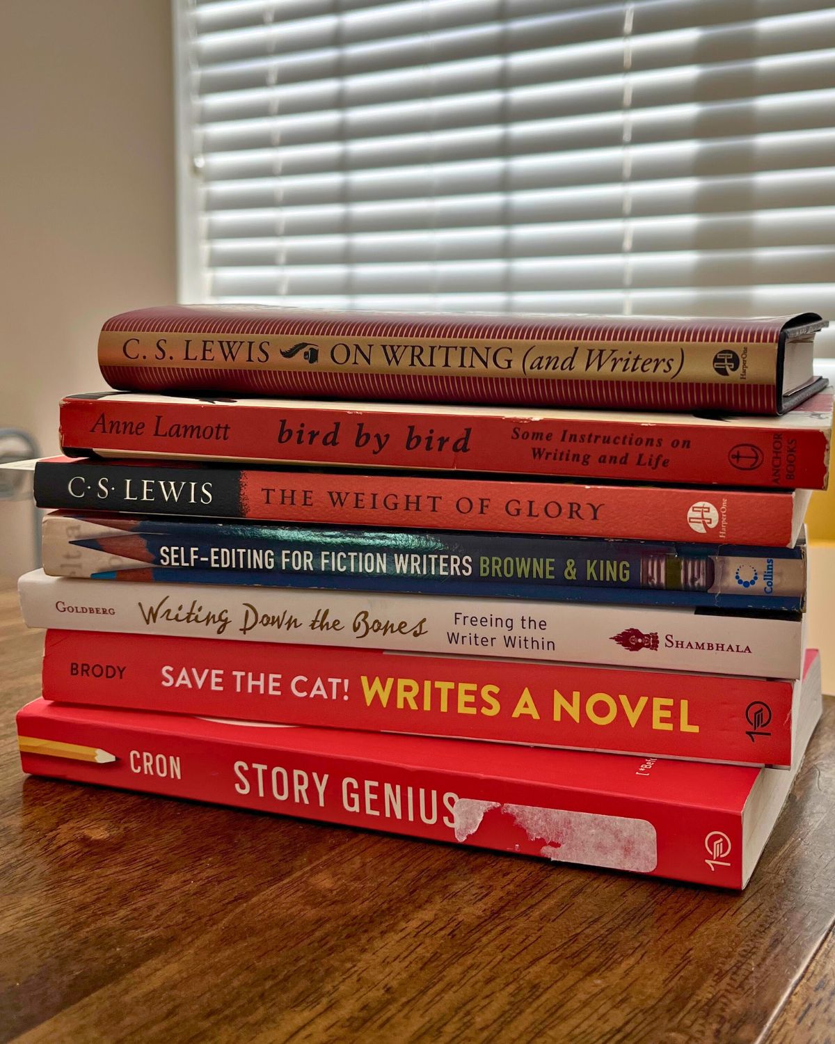 stack of writing books on wood table in front of window with blinds pulled.