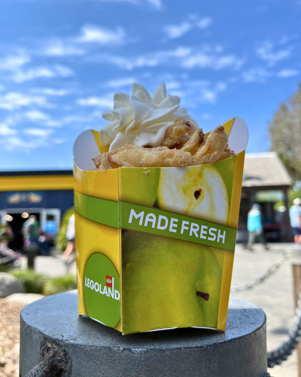carton of apple fries at legoland with blue skies and clouds behind.