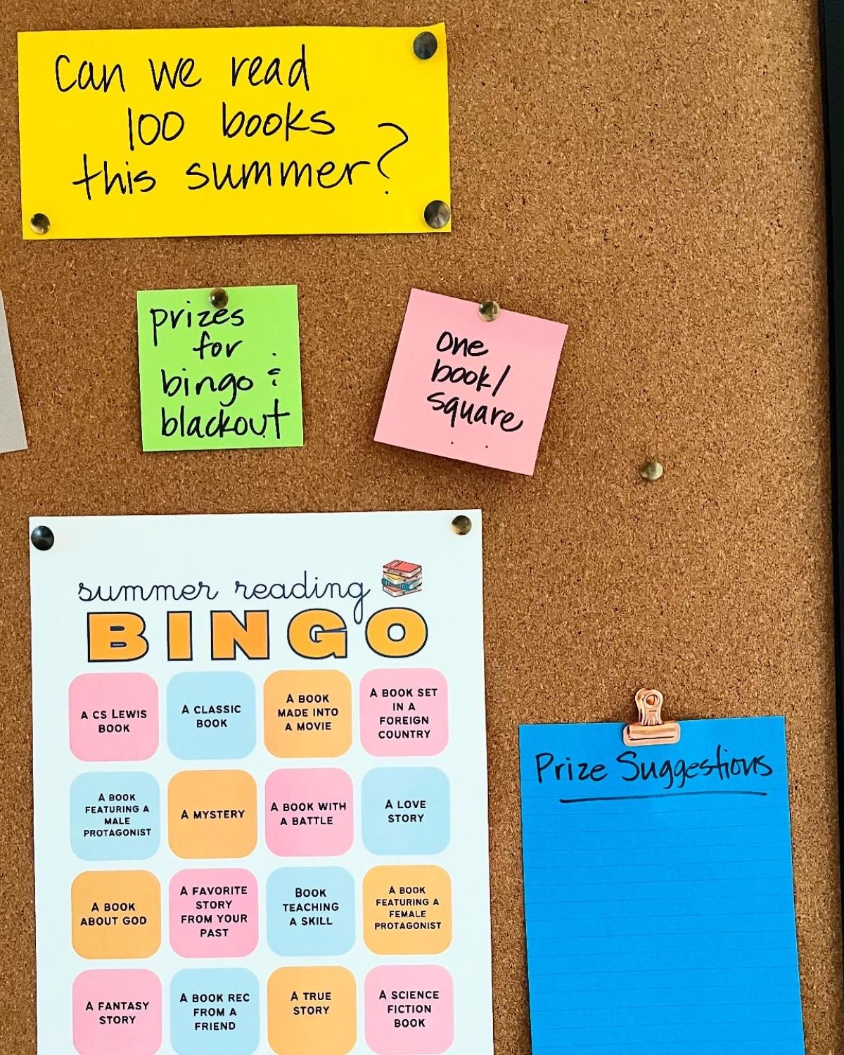 bulletin board with colorful notes, including summer reading bingo card.