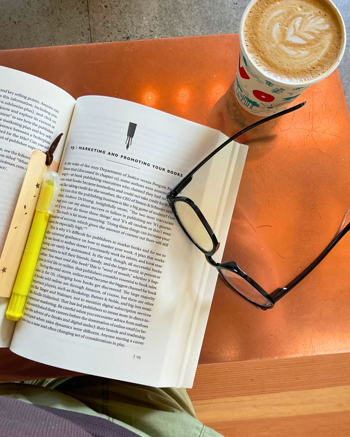 friedman book open to marketing chapter with highlighter, bookmark, glasses, and a coffee drink.