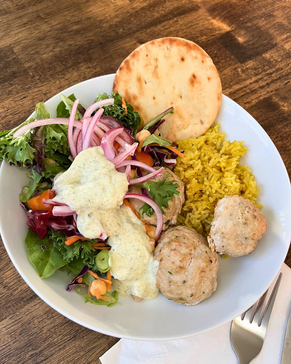 mediterranean bowl with chicken meatballs, salad, rice, naan, and yogurt sauce.