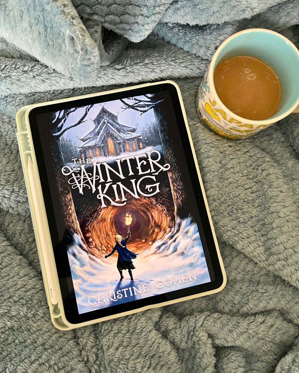 the winter king on iPad on a blanket with a cup of coffee.