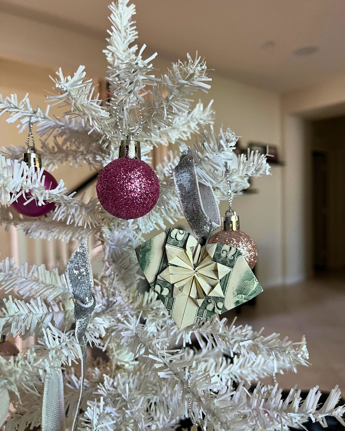 $2 bills turned into origami hearts serving as ornaments on mini christmas tree.