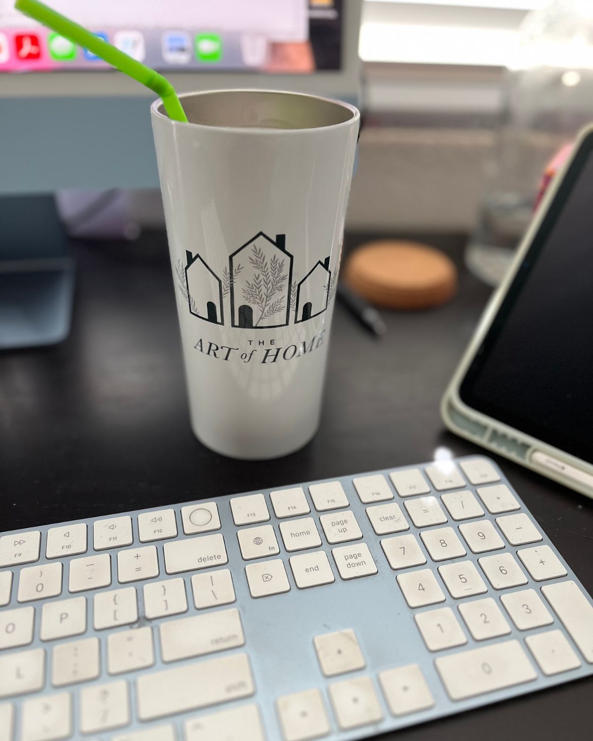 art of home cup on work desk with computer, iPad, and keyboard nearby.
