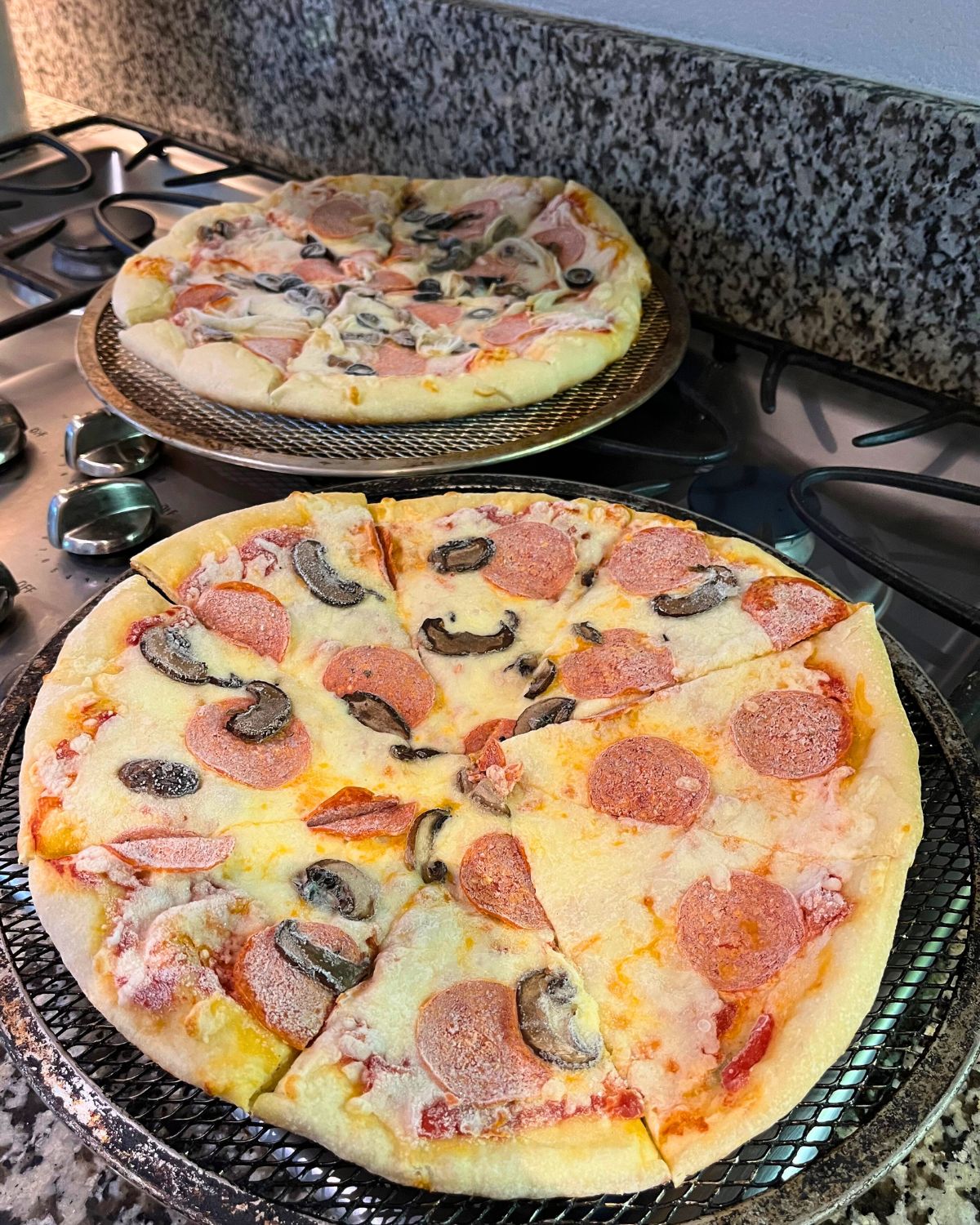 frozen pizzas on pizza screens waiting to be baked.