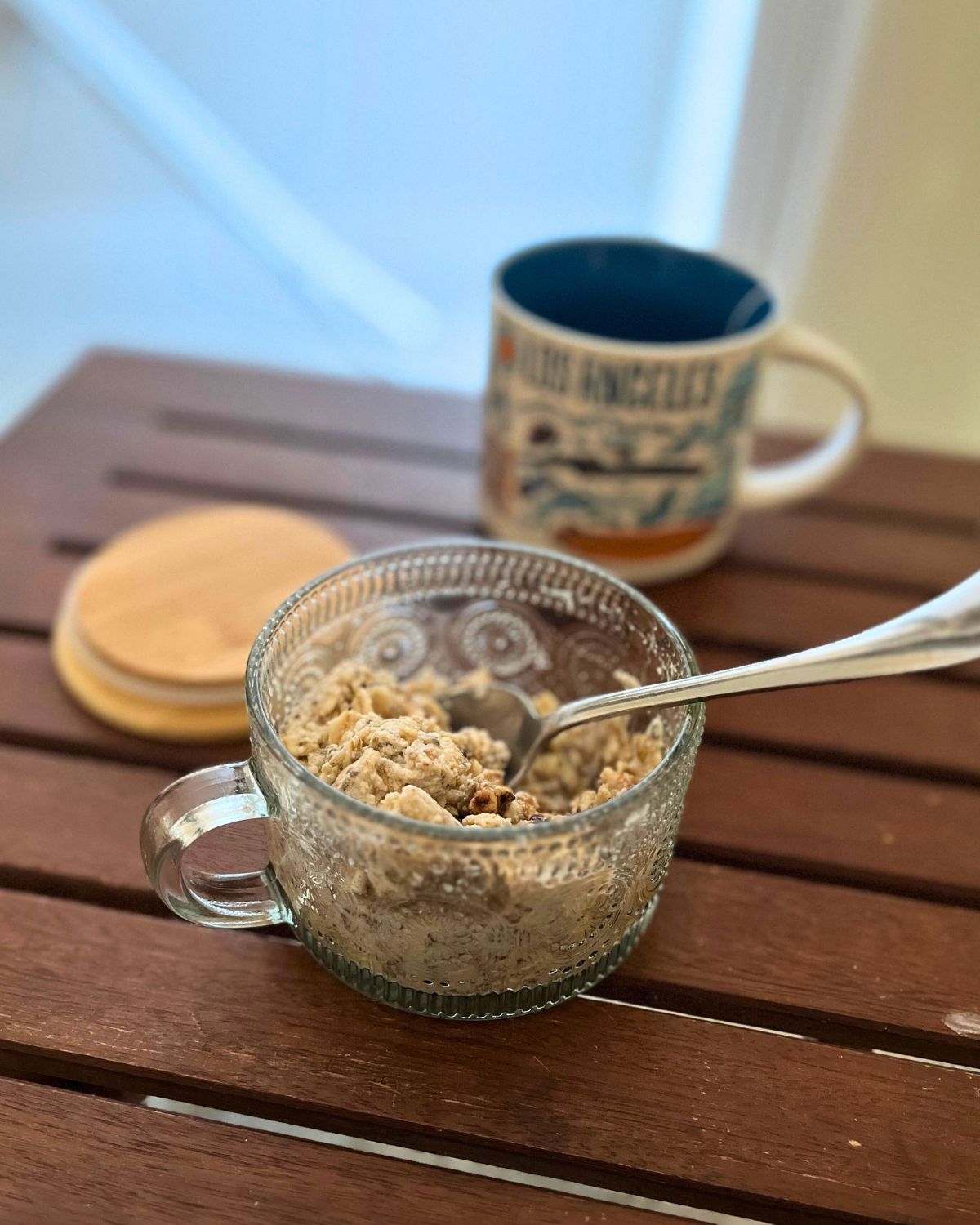 ornate glass mug with wooden lid filled with instant oats and a mug of tea and a spoon.