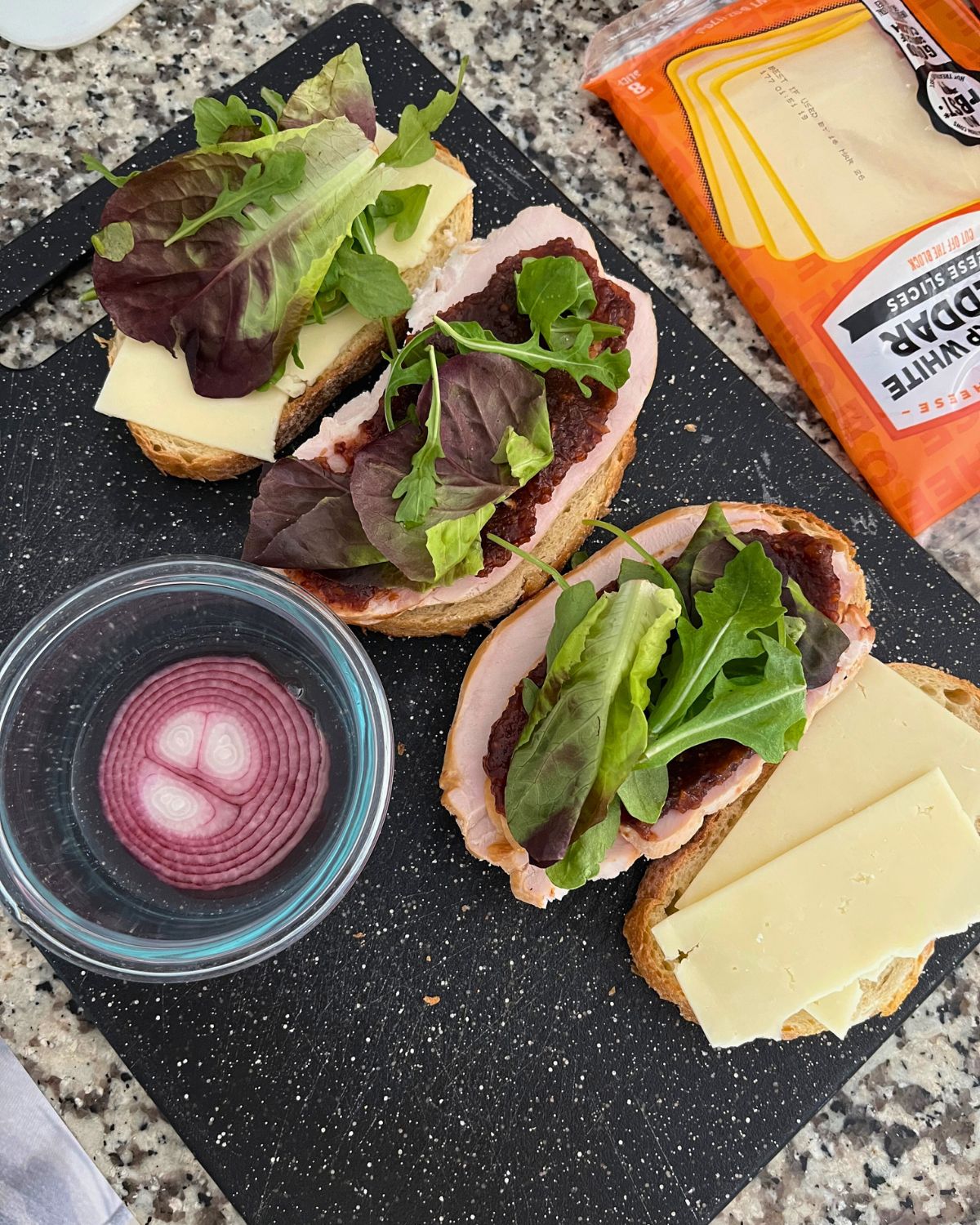 cheese and pickle sandwiches on board with pickled onions.