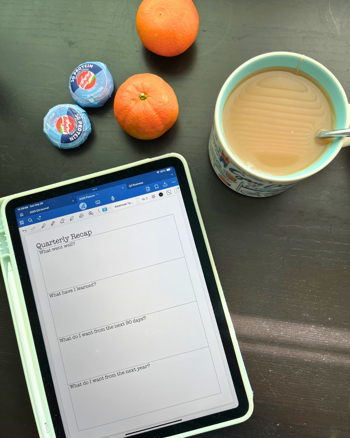 iPad showing quarterly recap page on table with oranges, snacking cheese, and tea in mug.