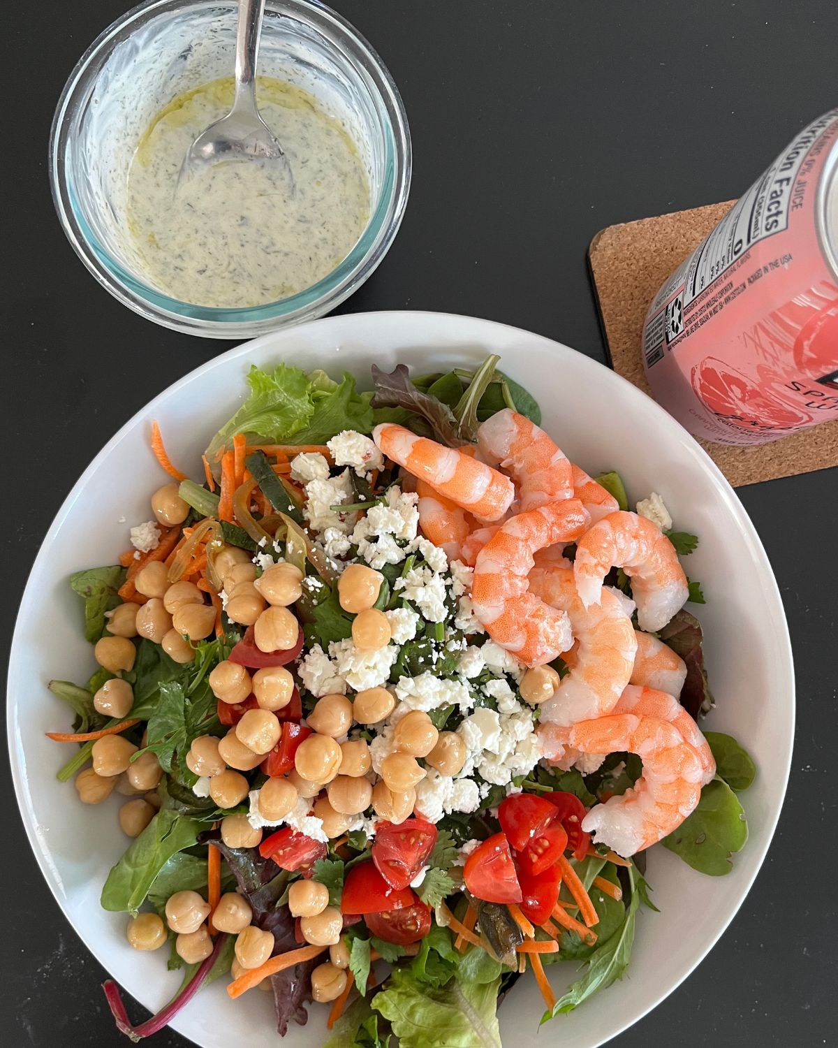 large lunch salad with shrimp next to a can of water and a dish of salad dressing.