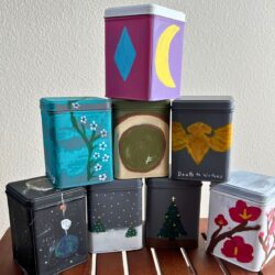 tea tins stacked on a wood table with a white background.