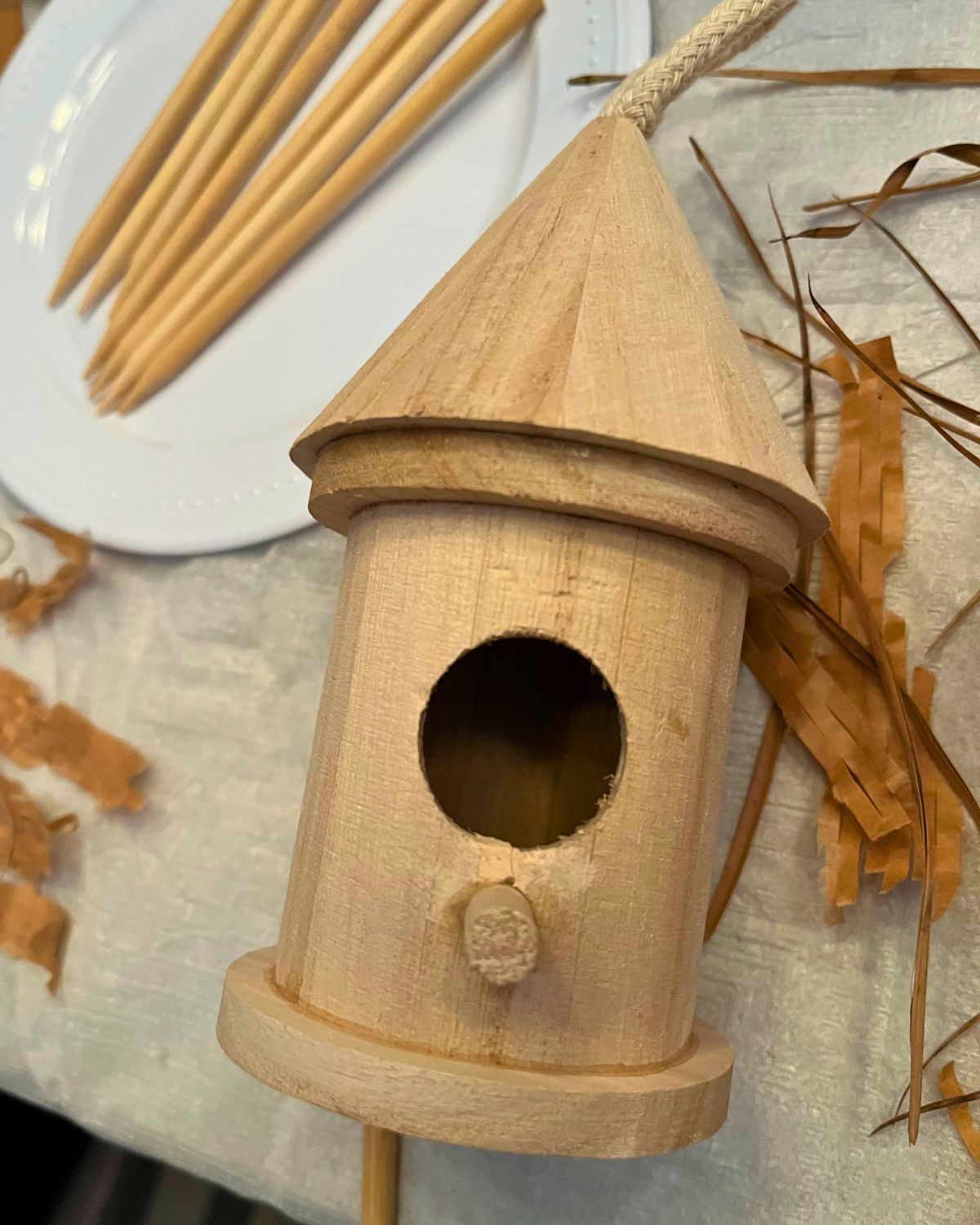 wooden round birdhouse on craft table surrounded by supplies.