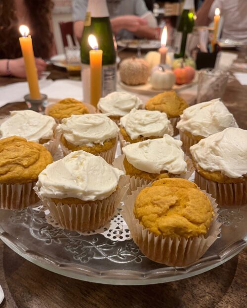 pumpkin cupcakes on cut glass platter with candles in the background.