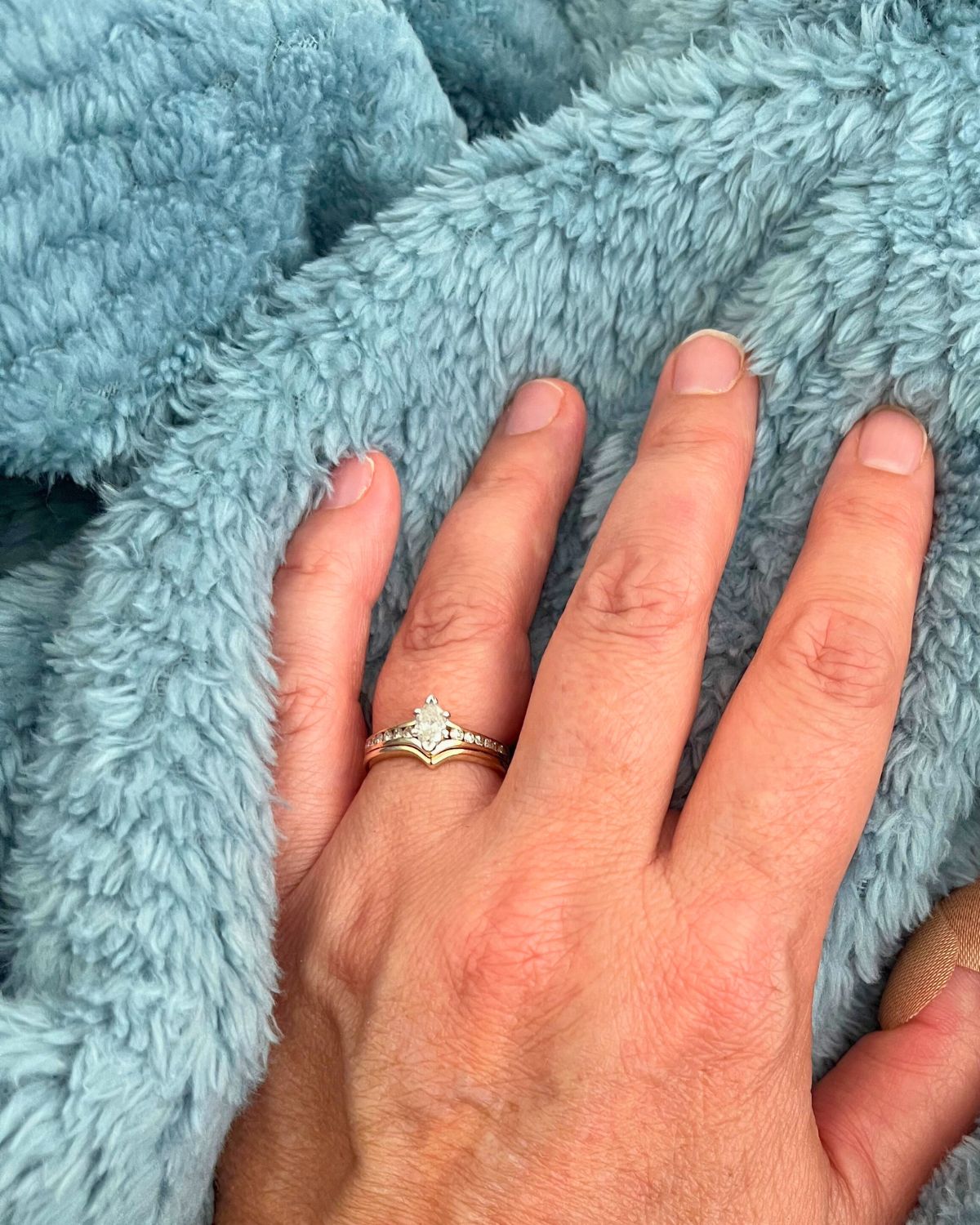hand on fuzzy blanket, with newly repaired diamond wedding set.